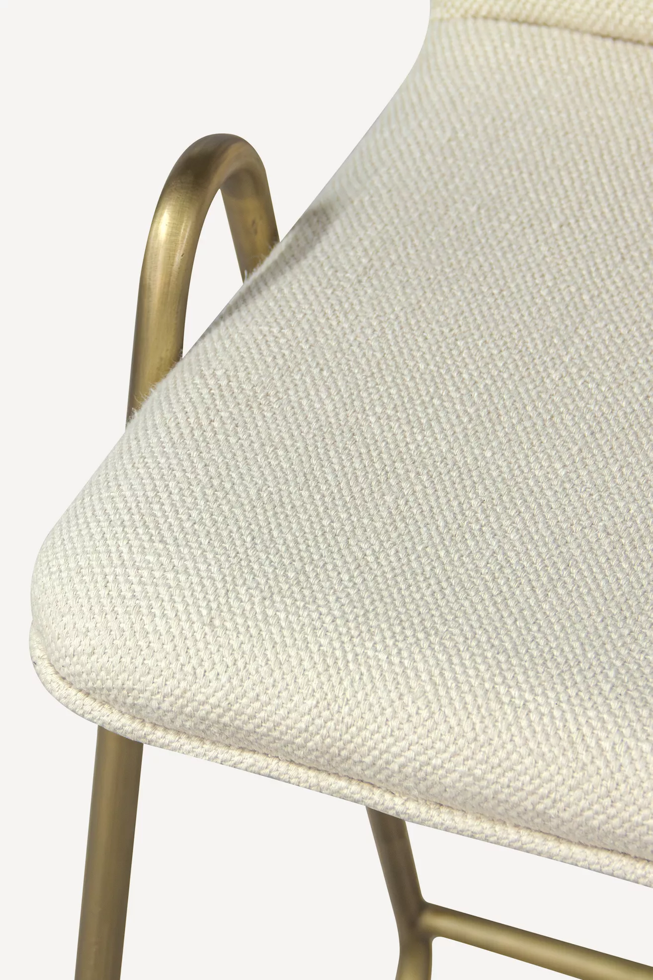 Close-up of cream textured upholstered counter stool cushion and brass-toned frame