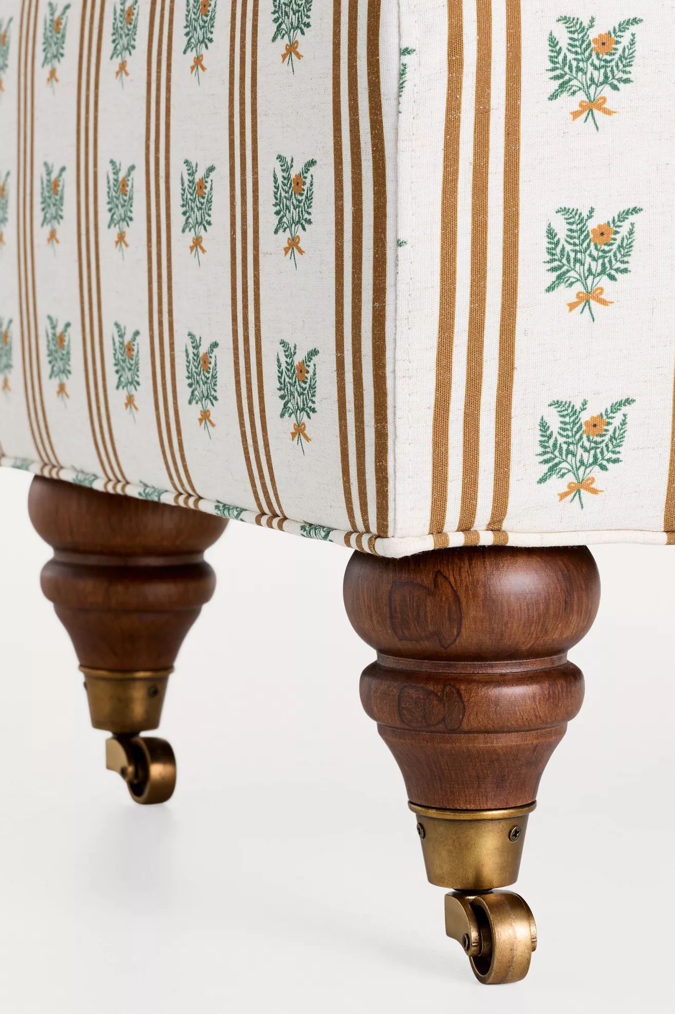 Close-up of wooden cabriole leg with brass caster on patterned upholstery