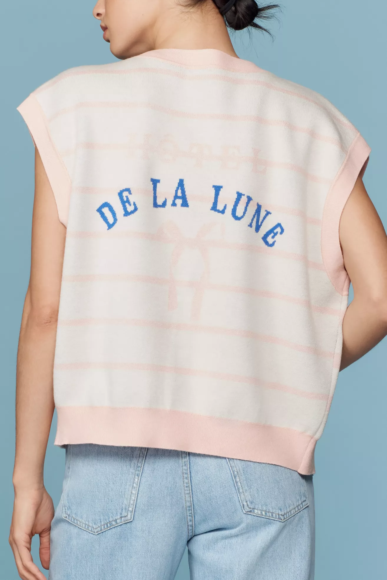 A white and pink stripe, button-up sweater vest, that says "De La Lune" on the back in blue text