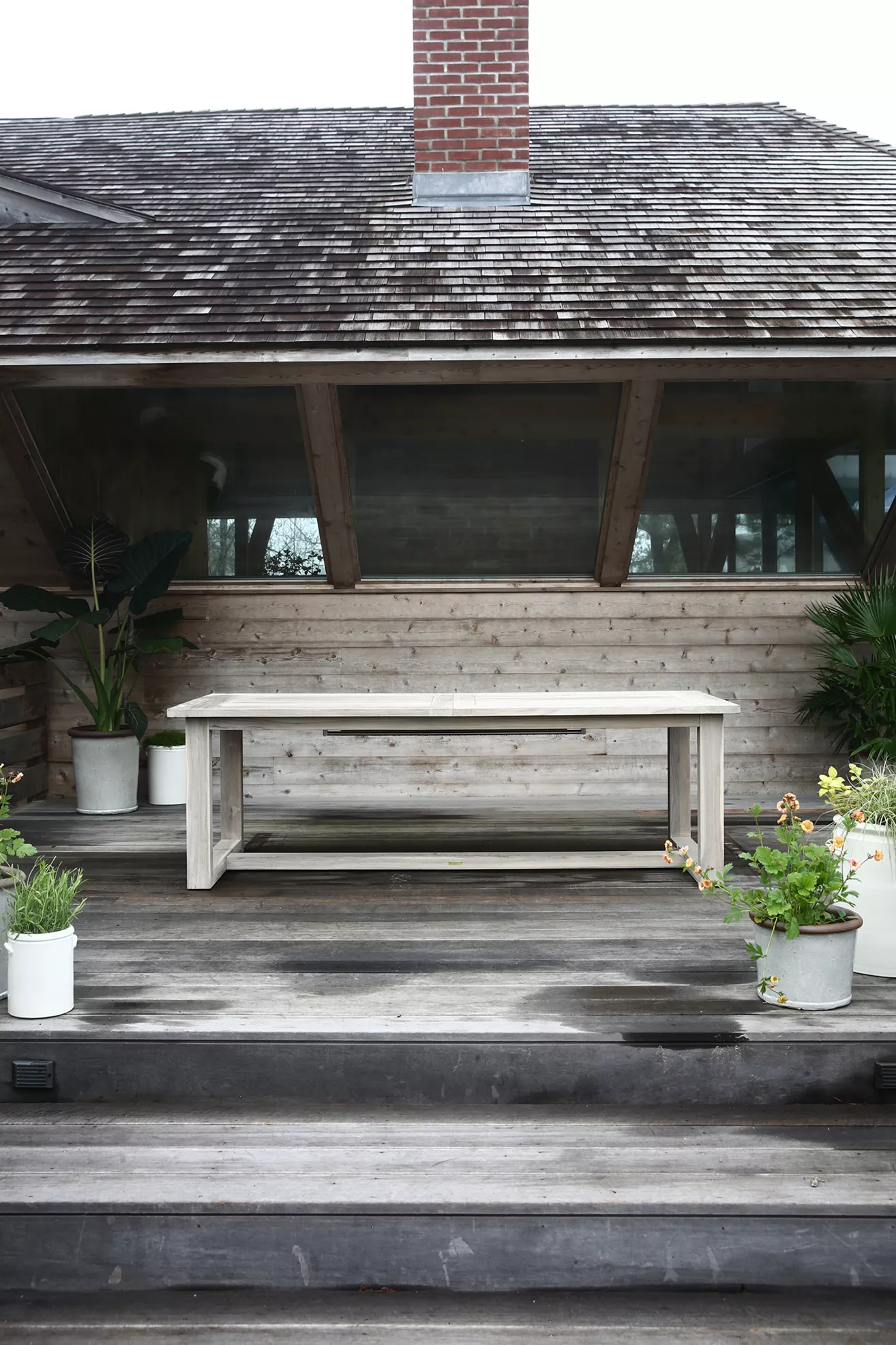 White teak extension table on a porch with potted plants