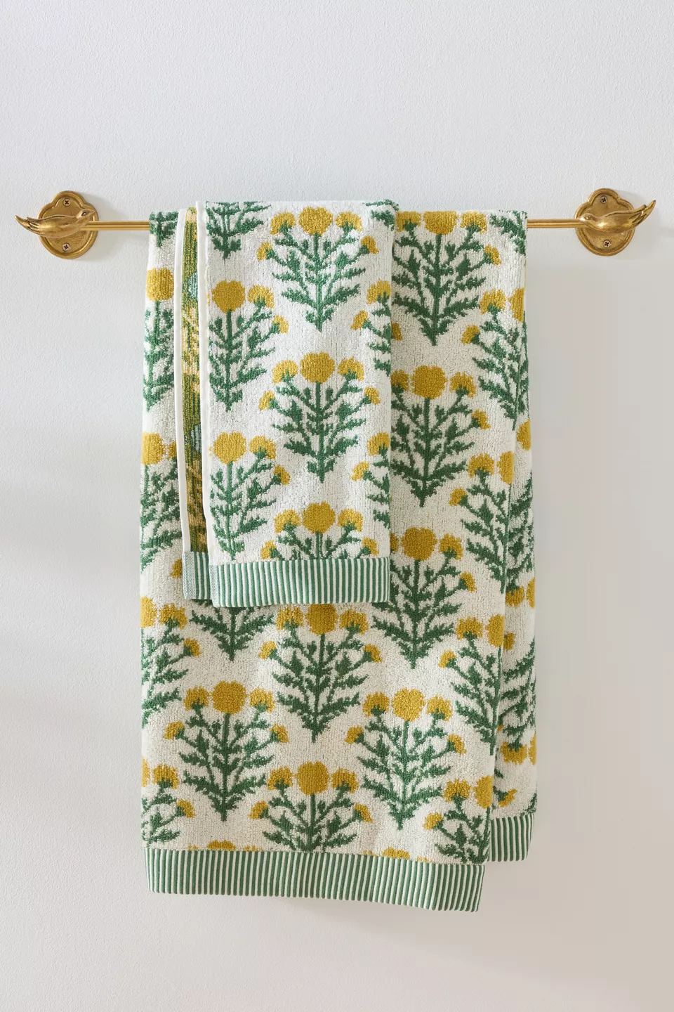 A large and small yellow, green, and white floral towel hanging on a gold rod