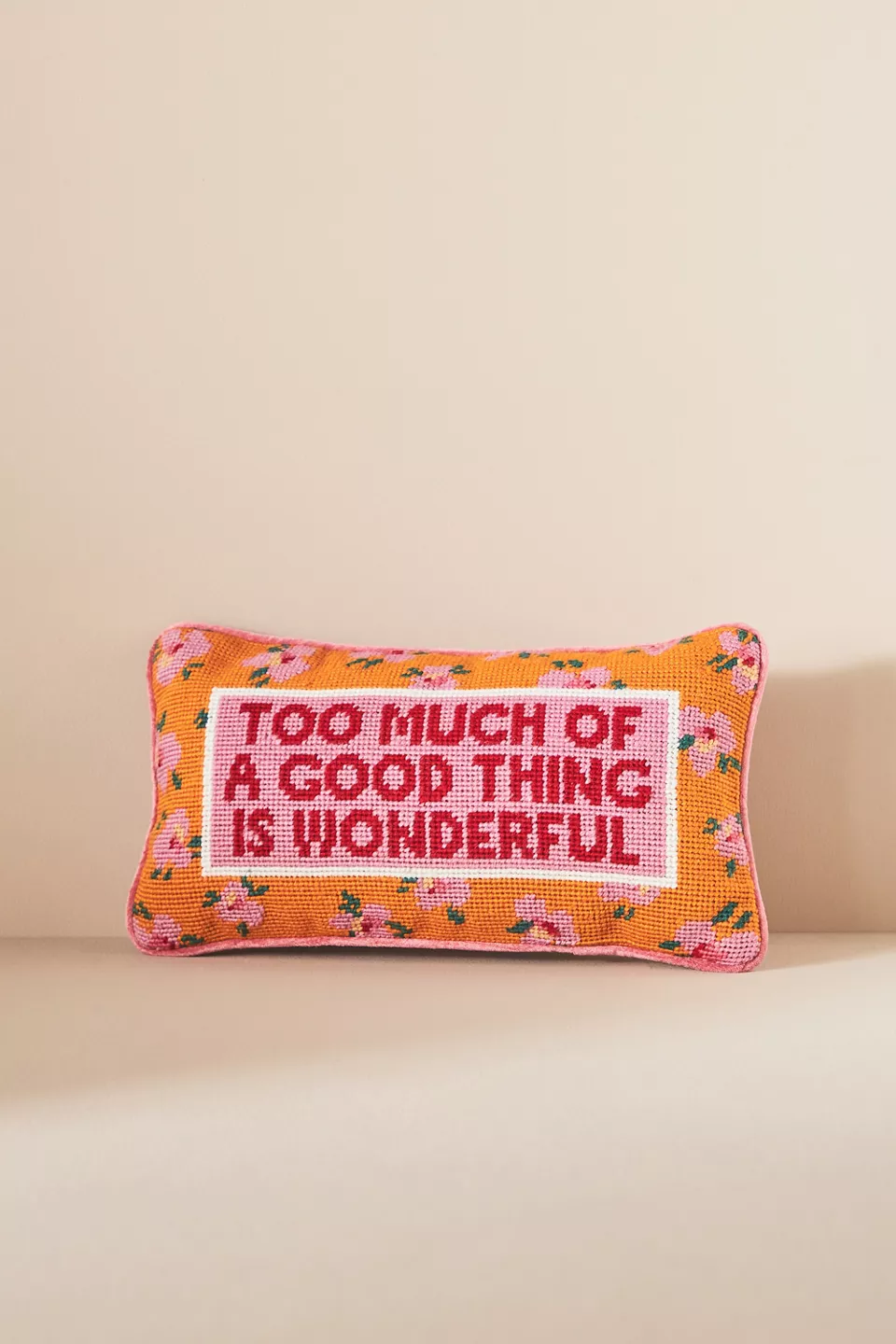 A pink, red, and orange needlepoint throw pillow with text