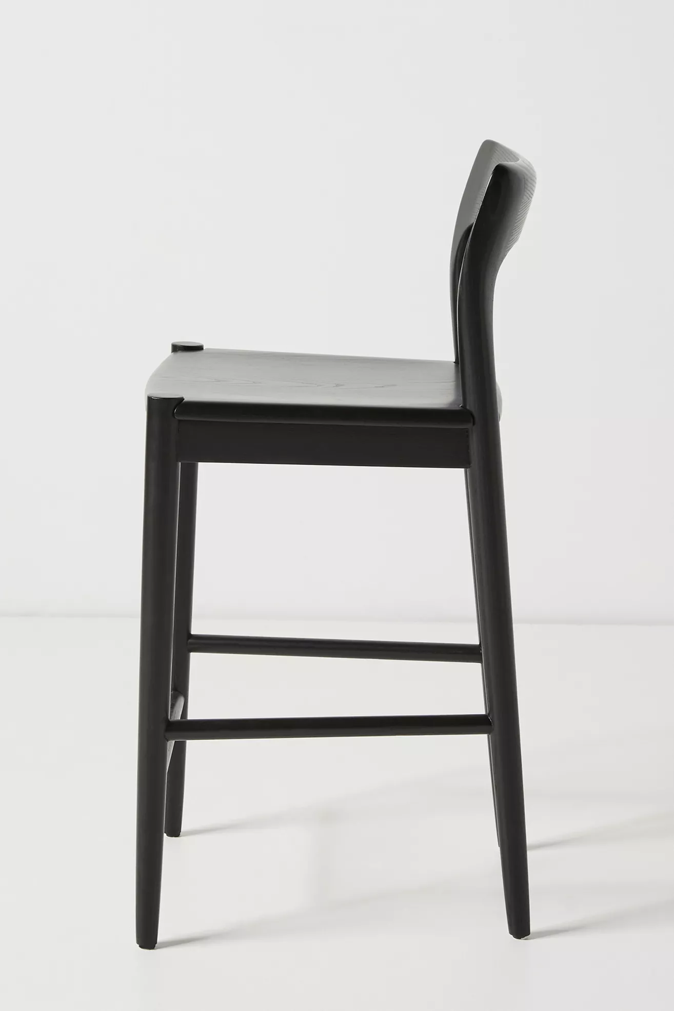 Side view of a black ash wood counter stool with straight legs and a slightly curved back