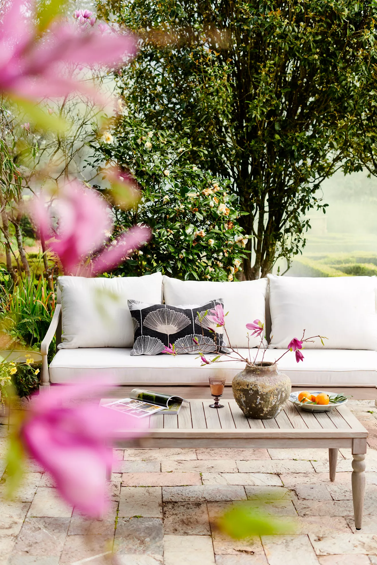 Teak three-seat outdoor sofa with white cushions and decorative pillows