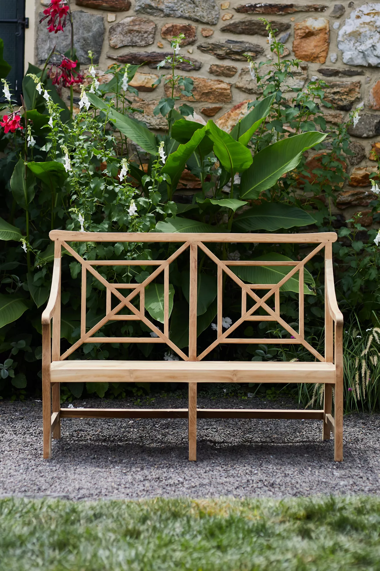 Full front view of two-seat fretwork teak bench against stone wall and plants
