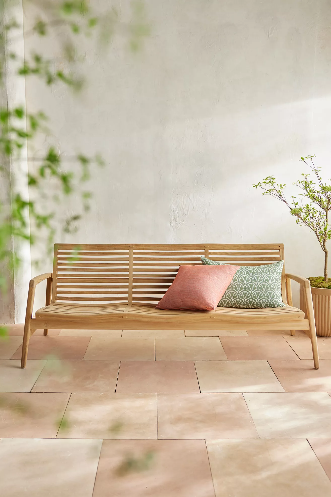 Teak slatted sofa with cushions against a white wall