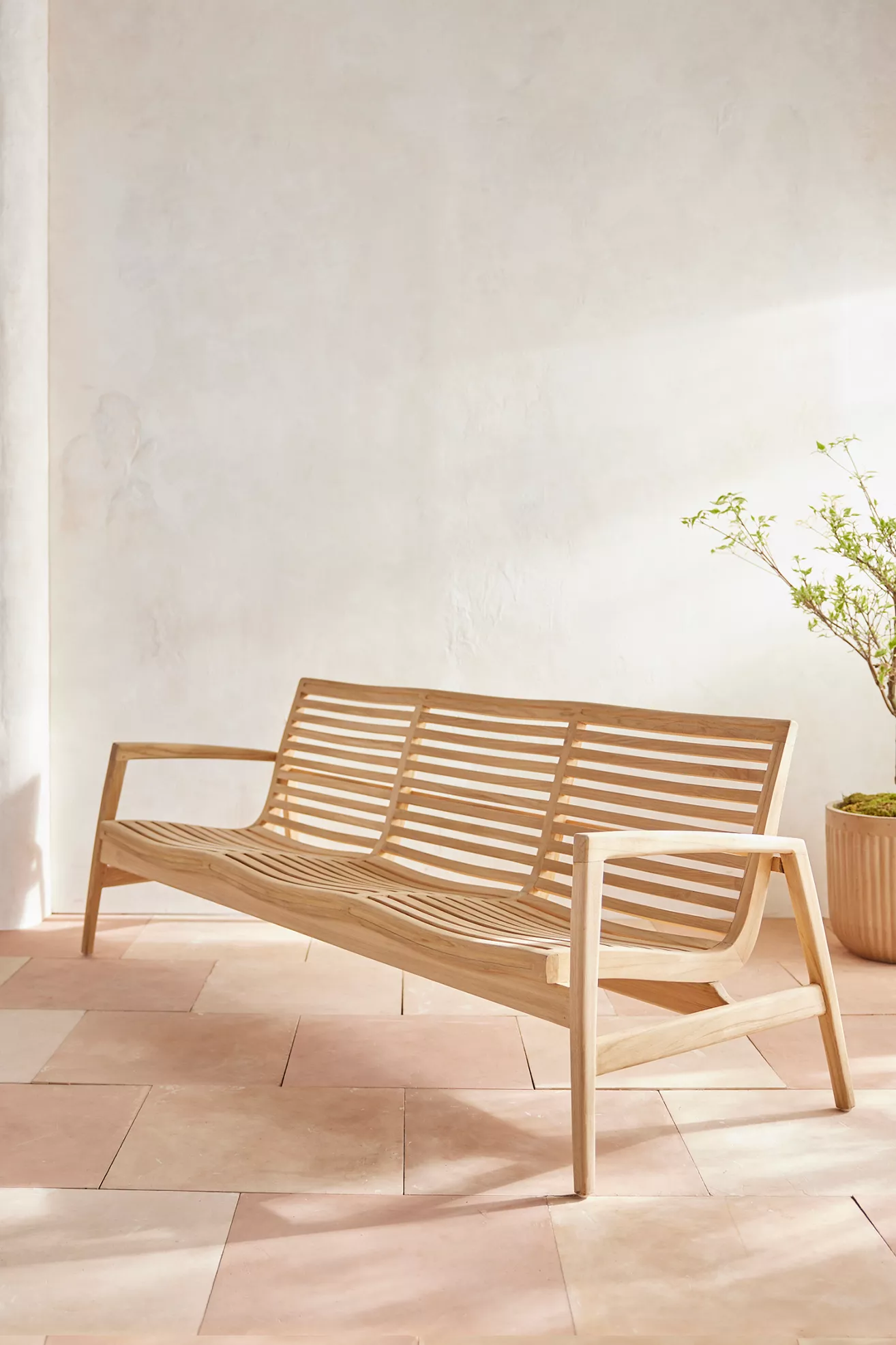 Teak outdoor sofa with armrests against light wall