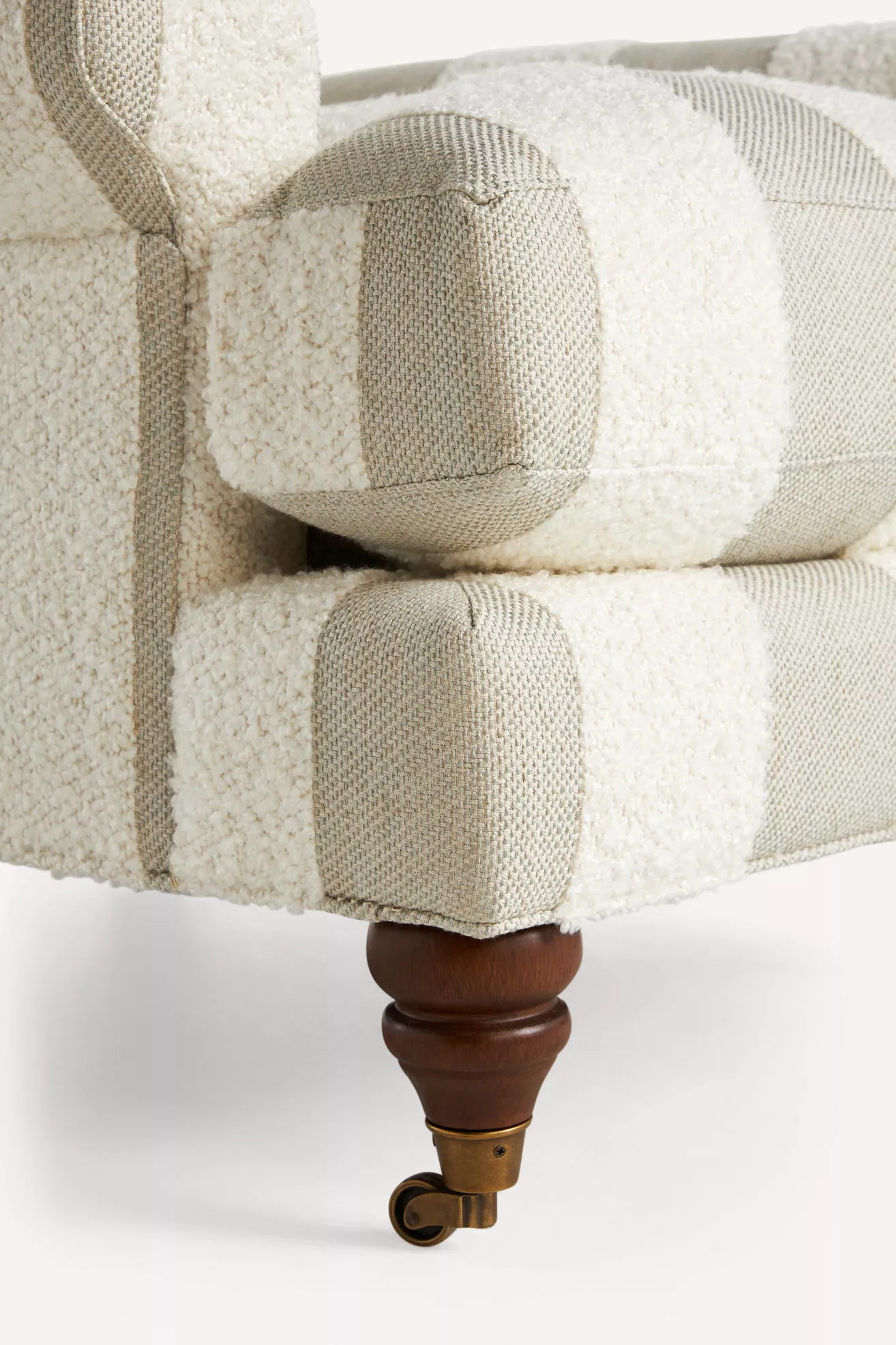Close-up of striped bouclé armchair arm with tufted cushion and turned wooden leg
