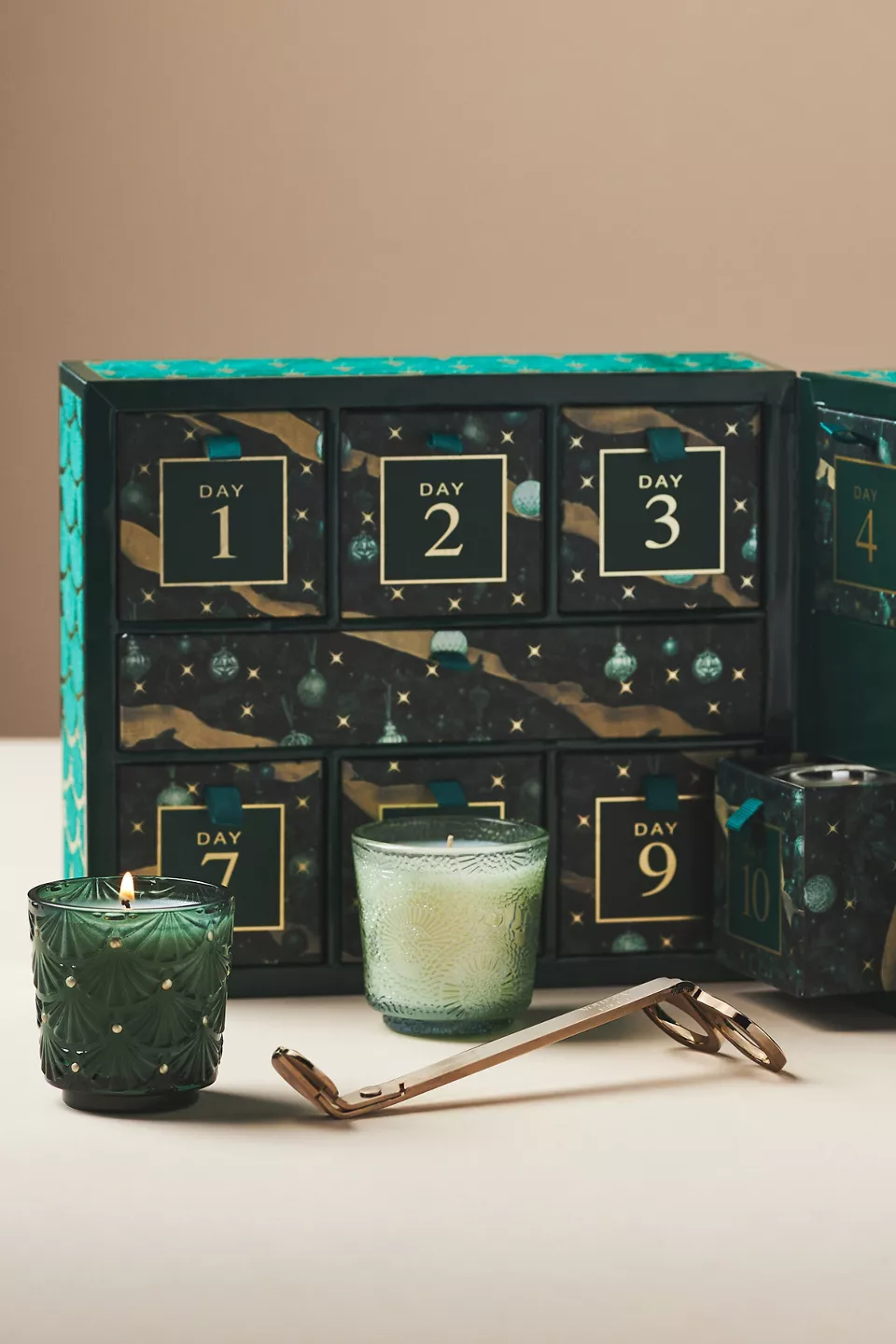 A green advent calendar with two candles and a wick trimmer in front of it