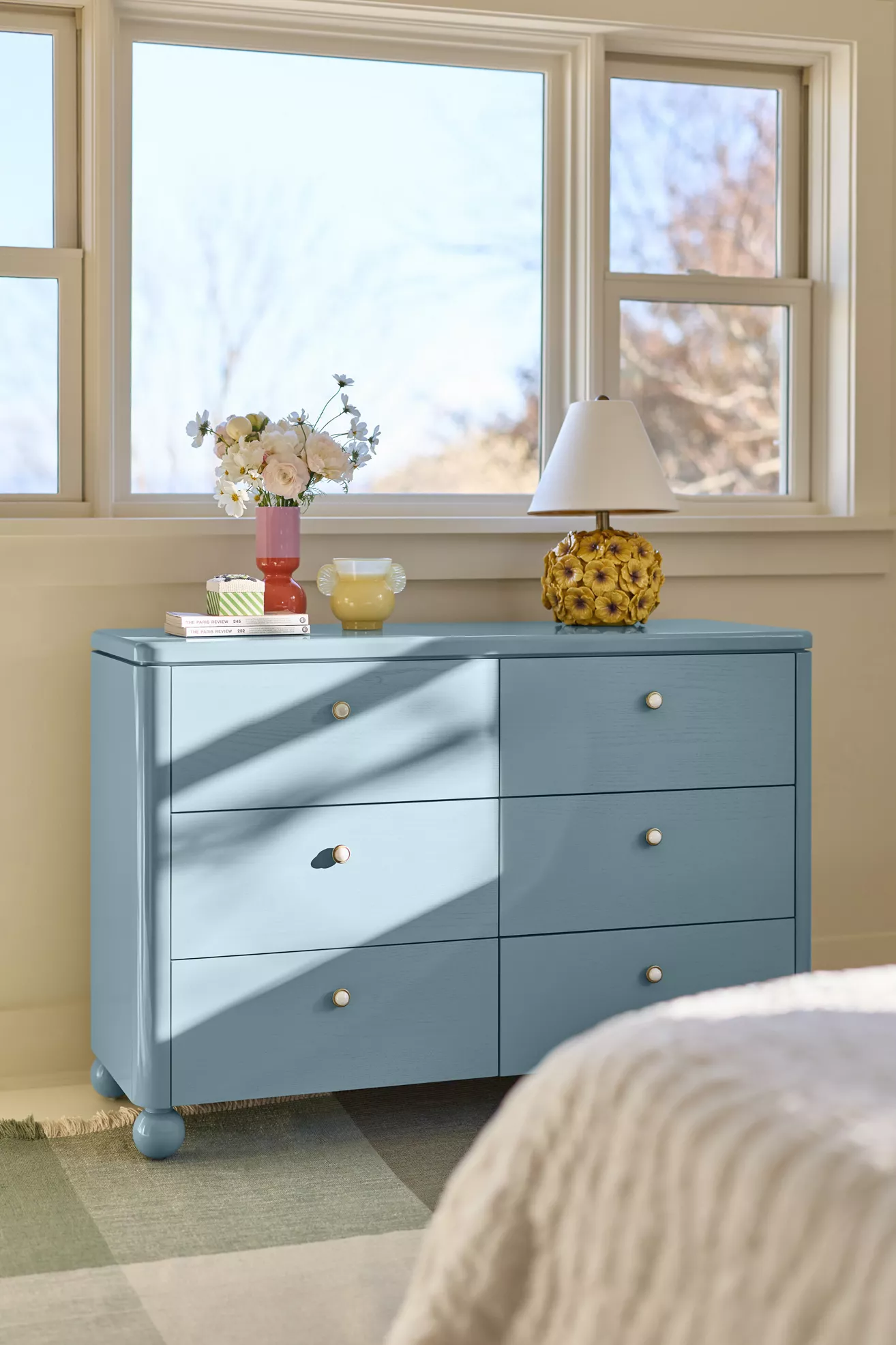 Blue dresser in sunlit bedroom with decor on top