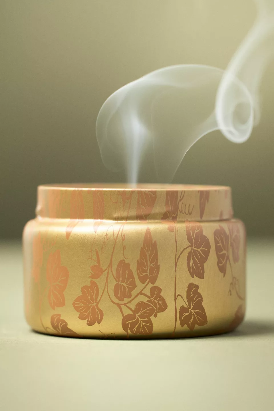 A gold candle tin with a leaf design on it