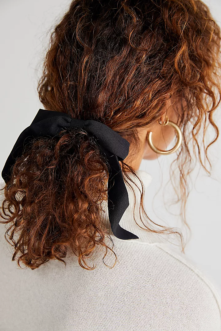 A small, black pony tail ribbon hair accessory on a woman with curly hair. 