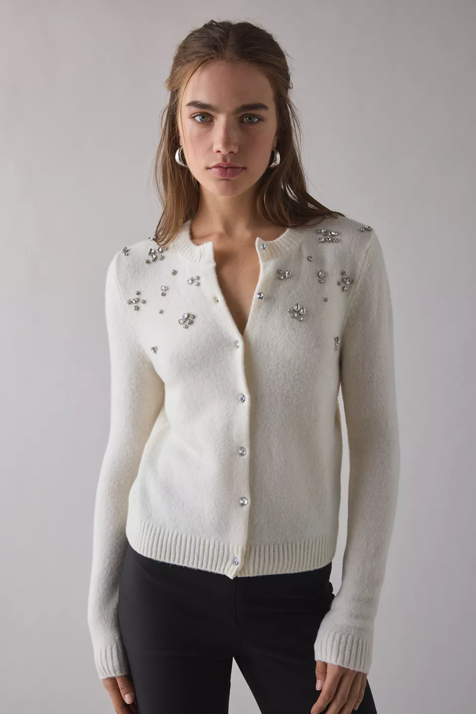 A woman wearing an ivory cardigan with silver gem embellishments on the top half