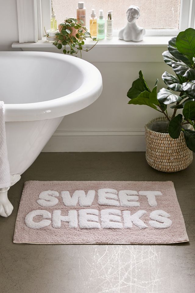 Pink bath mat that says "SWEET CHEEKS" on floor next to a white freestanding tub