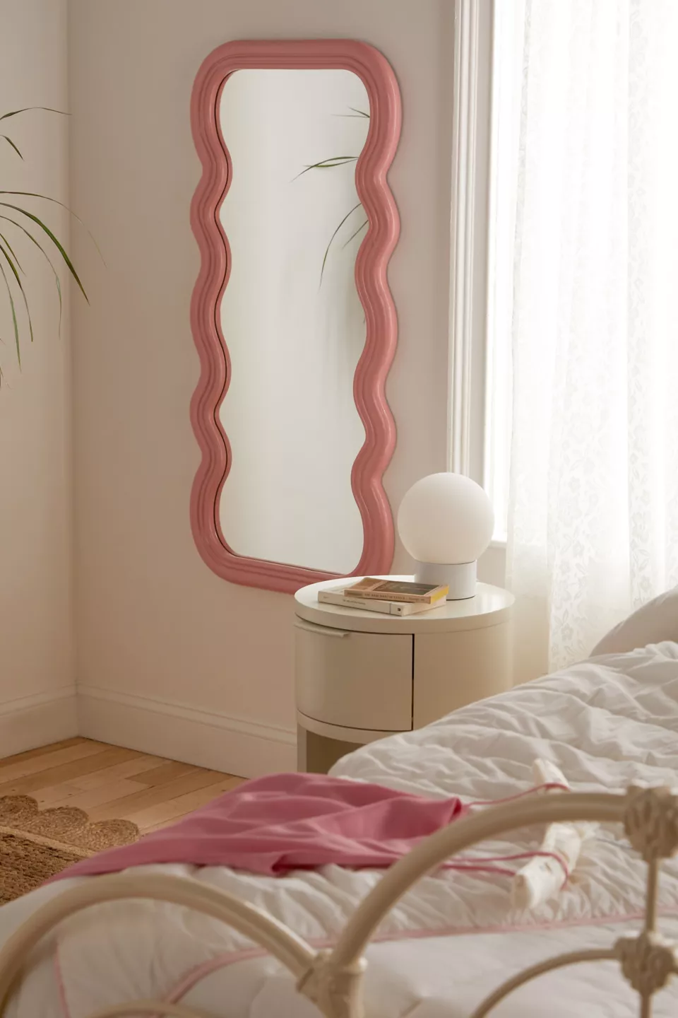 A pink wavy wall mirror hanging in a bedroom