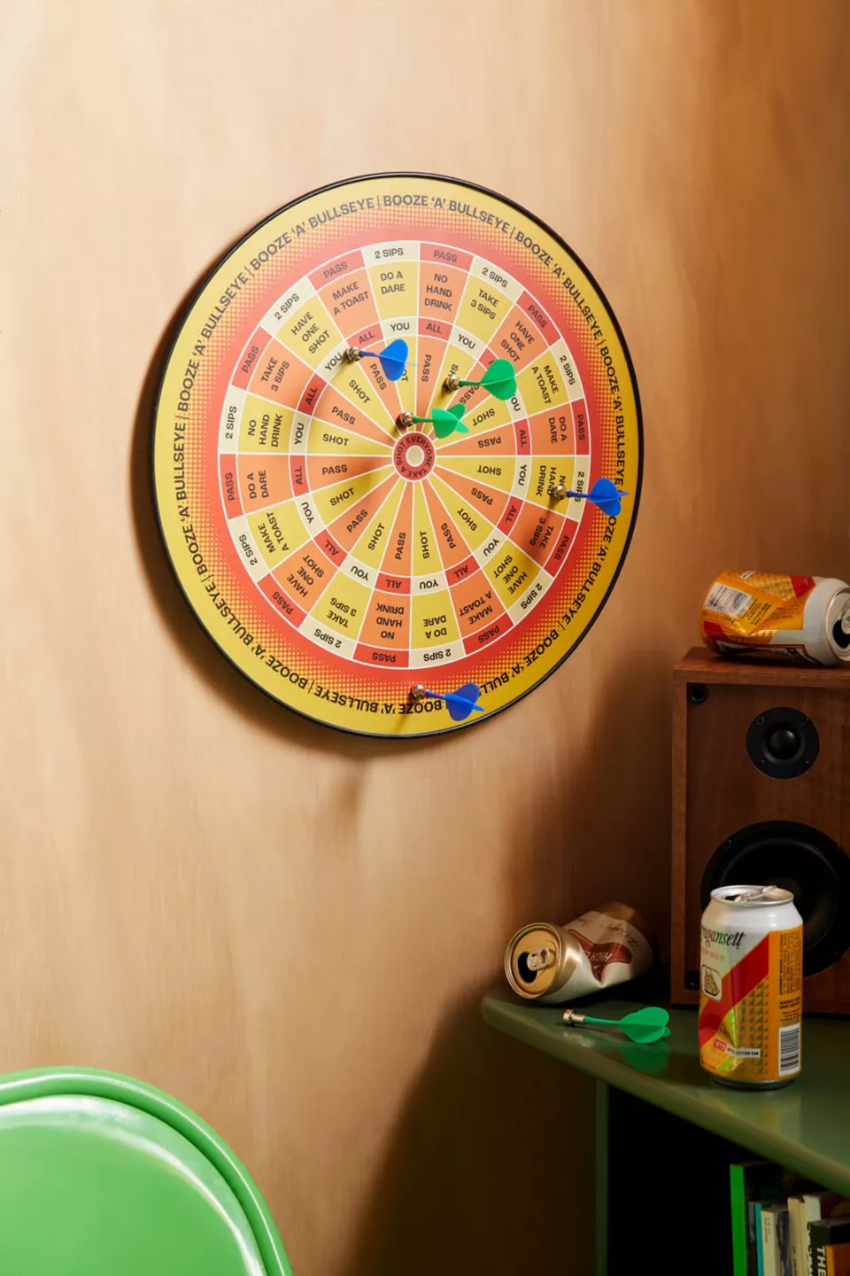 A yellow, red, and orange dart board on a wall with two green darts and three blue darts on it